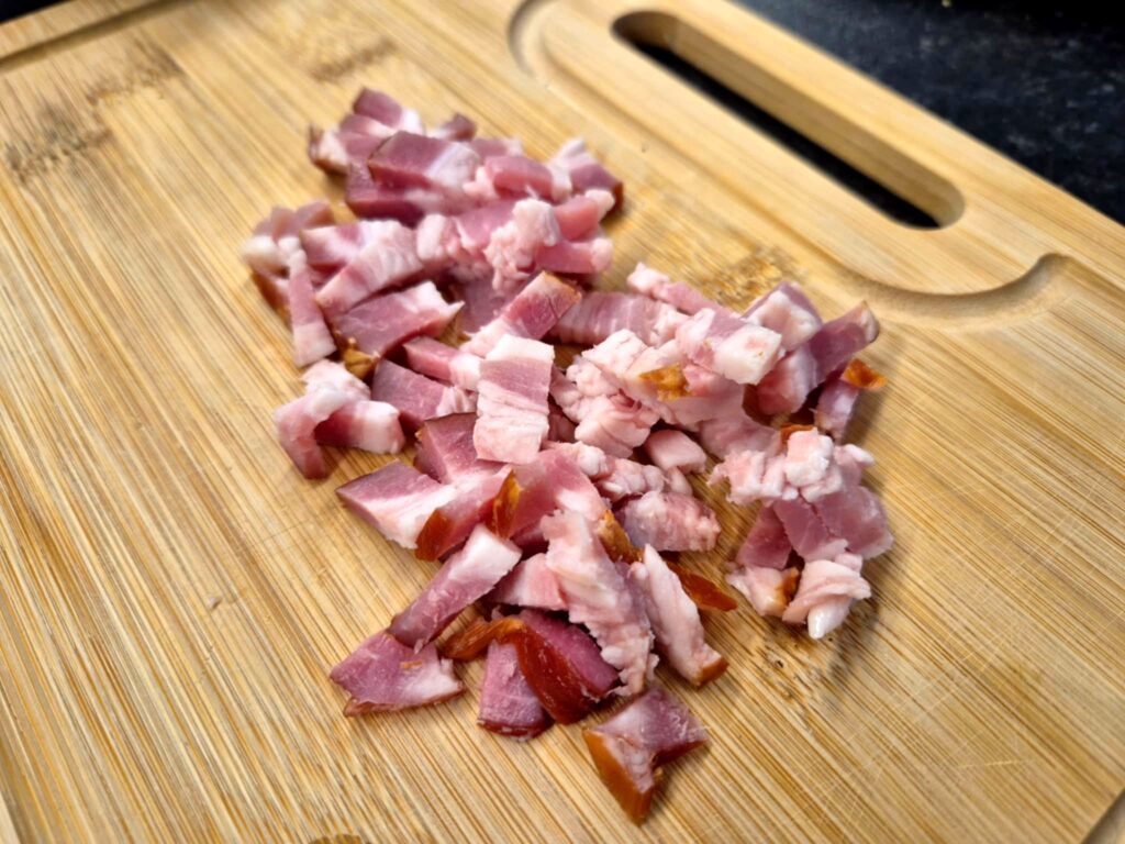Pokrojony w kostkę boczek na desce do krojenia, przygotowany do smażenia.