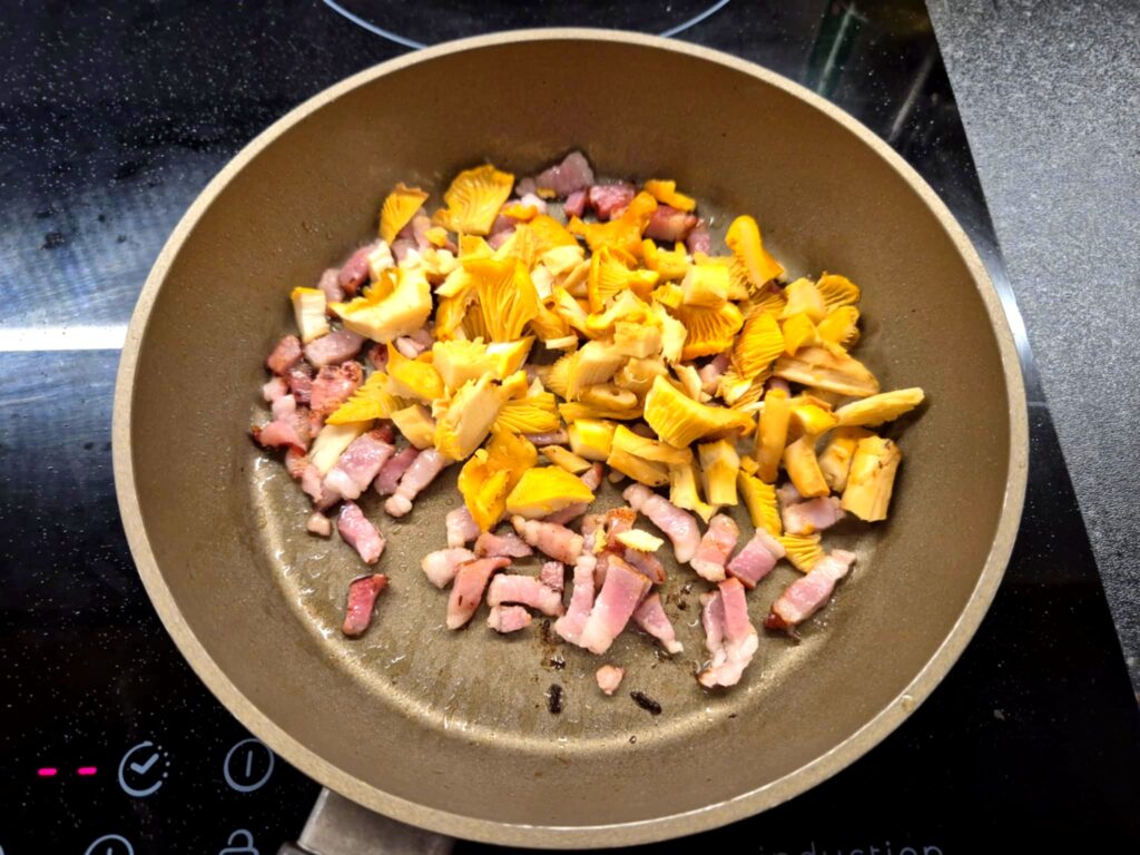 Podsmażany boczek z dodatkiem świeżych kurek na patelni.